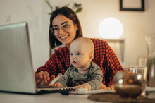 Beautiful Business Mom Using A Laptop And Spending Time With Her Baby Boy At Home