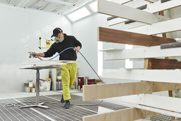 Painting at Right way. Man in respirator mask painting wooden planks at workshop