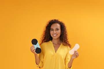 Wall Mural - Young African American woman with reusable menstrual pad and pantyliner on yellow background.