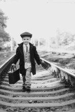 Child Boy In A Coat And With A Suitcase Walks On The Rails