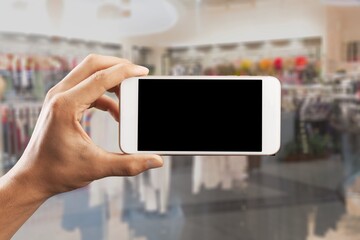 Sticker - Online shopping concept. Hands holding mobile phone on blurred store as background