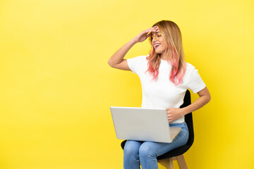 Young woman sitting on a chair with laptop over isolated yellow background smiling a lot