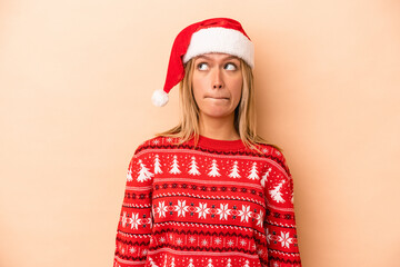 Wall Mural - Young caucasian woman celebrating Christmas isolated on beige background confused, feels doubtful and unsure.