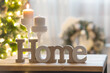 © Юлия Клюева - The word home and burning candles in white candlesticks in the interior of the living room on the background of a Christmas tree.The concept of winter, festive home comfort and warmth.