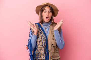 Wall Mural - Young caucasian fisherwoman holding a net isolated on pink background surprised and shocked.