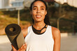 © Drobot Dean - Black sportswoman smiling while standing with fitness mat on parking
