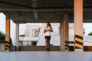 Wall Mural - Black sportswoman listening music while running on parking