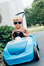 Bored Blond Boy Wearing Sunglasses Sitting In Blue Toy Car