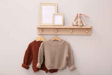 Poster - Wooden shelf with child's clothes, toy bunny and photo frames on beige wall. Interior element