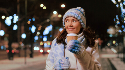 Poster - winter holidays, christmas and people concept - happy smiling young woman drinking takeaway coffee on city street at night