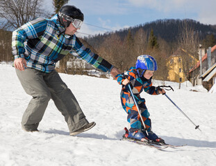 child boy learns to ski with his father during winter vacation in snowy mountains on sunny cold day. Winter active walks with children. Seasonal joys, happy childhood. Sports education, care, support