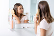 © Syda Productions - beauty and people concept - teenage girl looking to mirror and brushing wet hair with comb at home bathroom
