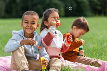 Childhood, Leisure And People Concept - Group Of Children Blowing Soap Bubbles At Park