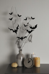 Poster - Alarm clock, burning candles and vase with paper bats  on table near white wall. Halloween decor