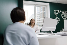 Smiling Saleswoman Talking To Client At Desk In Travel Agency