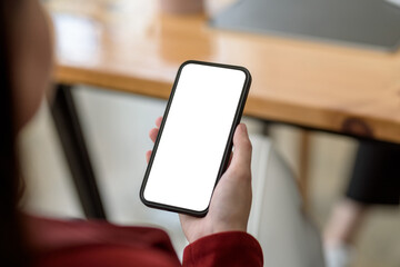 Woman sitting holding a smartphone blank white screen at café. Mock up