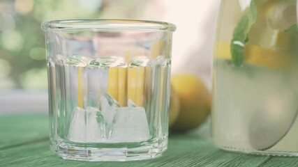 Wall Mural - Fresh cold lemonade with mint and ice, outdoors shot. Ice falls into a glass.