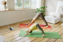 Mother And Daughter Doing Downward Facing Dog Posture At Home