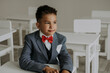 © Westend61 - Schoolboy wearing red bow tie with suit sitting in classroom
