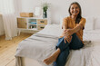 © shurkin_son - Laughing elderly woman in perfect mood, posing with legs crossed holding one knee in arms in front of camera at home against bedroom interior background, dressed casually, looking gorgeous