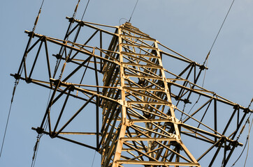 Wall Mural - Part of  transmission tower (power tower) with powerful steel frame and high-voltage wires, angled view, sunny day, blue sky background