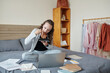 © DragonImages - Young woman sitting on bed with documents around, eating lunch and reading documents and e-mails on laptop screen