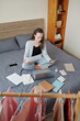 © DragonImages - Positive businesswoman sitting on bed at home and working with documents, view from above