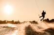 © fesenko - silhouette of male rider holding rope and making extreme jump on wakeboard over splashing water.