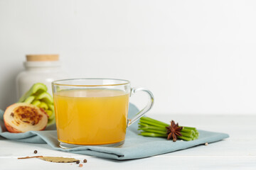 Homemade vegetable or meat broth in a glass mug, on a light background, with baked onions and herbs. Close-up