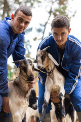 vertical portrait of two young livestock farmers with their goats in their farmyard. concept of young people working in livestock and agriculture