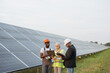 © sofiko14 - Muslim woman in hijab and indian man in white helmet talking with african american technician on solar station. Multiracial people using laptop, clipboard and blueprints for work outdoors.