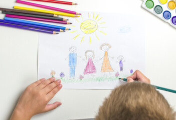 The boy draws a family with colored pencils. Happy family concept.