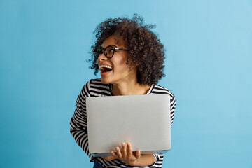 Wall Mural - Cheerful Afro American lady looking away and smiling while holding notebook. Isolated on blue background