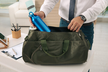 Wall Mural - Businessman packing sports stuff for training into bag in office, closeup