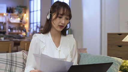 portrait serious female manager wearing headset is having video conference on notebook online. explaining to clients with hand gestures and paper.