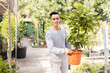 Smiling young male florist carrying potted Aucuba japonica with colorful spotted leaves in sunny greenhouse