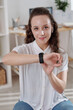 © DragonImages - Portrait of smiling young woman checking notification on smartwatch and looking at camera