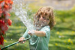 Happy little boy having fun in domestic garden. Child hold watering garden hose. Active outdoors games for kids in the backyard during harvest time
