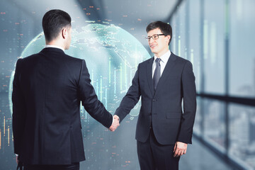 Canvas Print - Two attractive young european businessmen shaking hands in blurry office interior with glowing globe hologram. Teamwork and globalized business concept. Double exposure.