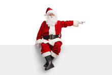 Santa Claus Sitting On A Blank White Banner And Pointing To The Side