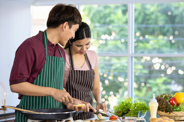 Romantic young Asian lovers happy talking, enjoy cooking healthy food together by spreading butter on toasted bread, chopping organic onion on cutting board on kitchen table of frying pan