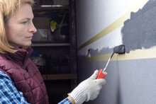 Female Painting A Wall With Masking Tape And Roller