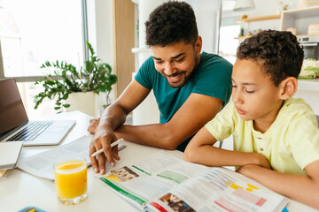 Father sitting at the dining table with his beloved son and helping him with the homework.