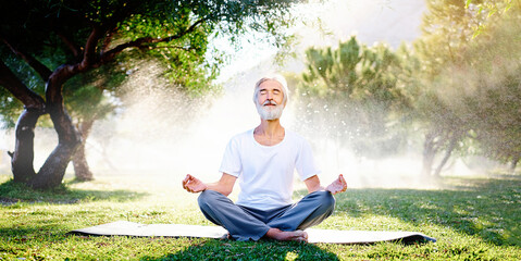 Wall Mural - Yoga at park. Senior bearded man in lotus pose sitting on green grass. Concept of calm and meditation. Horizontal photo banner for website header design
