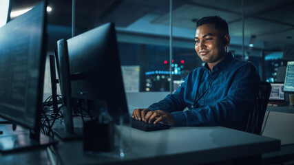 Poster - Night Office: Portrait of Handsome Indian Man in Working on Desktop Computer. Digital Entrepreneur Typing, Creating Software, e-Commerce App Design, Programming. Thoughtful Happy Man Finding Solution