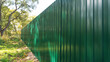 A corrugated fence of green metal sheets with screw. Texture of metal fence picket Profile decking. Internal primed side of a metal picket fence