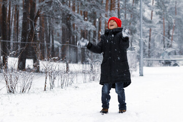 Wall Mural - A boy in a red hat happily throws snow up in the winter forest