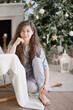 © Dina - Beautiful young woman near christmas tree in the living room. Woman at home decorated for winter holiday season.