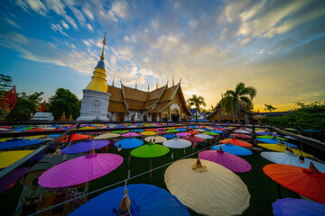 Wall Mural - Northern Thailand Temple on Loi Krathong day (Yi Peng Festival) with many colored umbrellas in the foreground in sunset.