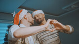 Fototapeta Londyn - Christmas spirit in a gay family. Homosexual couple making heart shape with hands in front of chistmas tree. High quality photo
